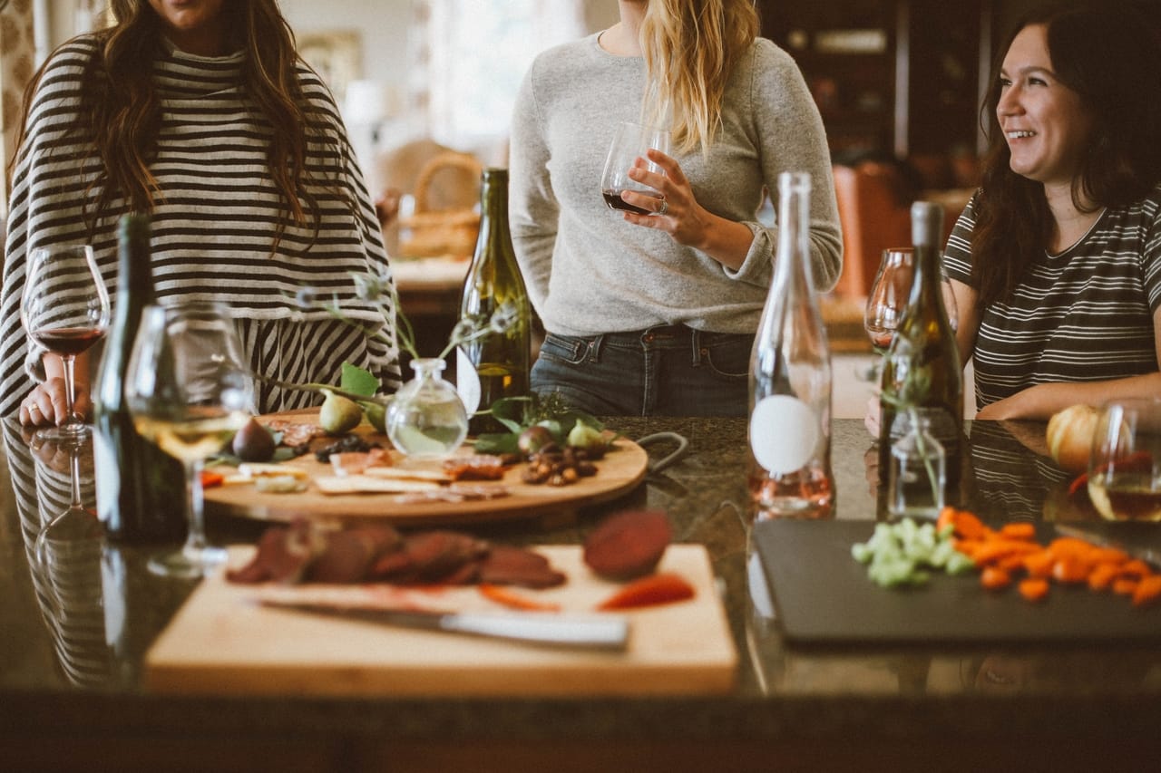 three women gathering around a table that's filled with food and wine