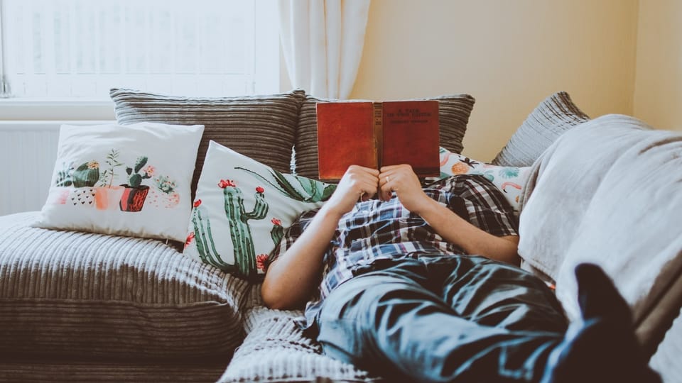man-reading-book-laying-on-couch